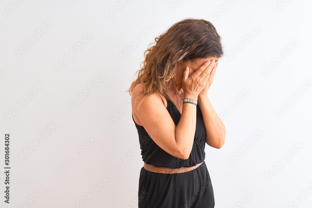 Middle age woman wearing black casual dress standing over isolated white background with sad expression covering face with hands while crying. Depression concept. Middle age woman wearing black casual dress standing over isolated white background with sad expression covering face with hands while crying. Depression concept.