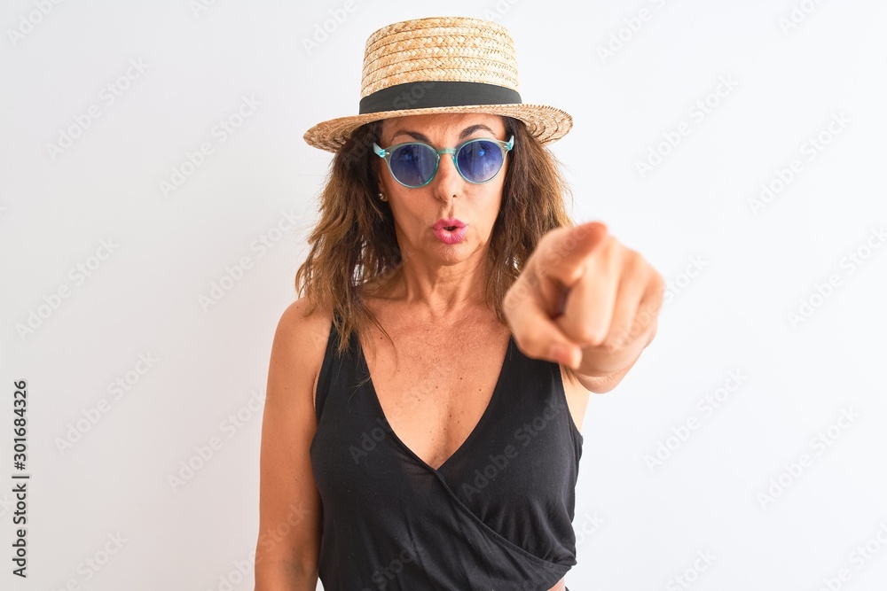 Middle age woman wearing black t-shirt sunglasses and hat over isolated white background pointing with finger to the camera and to you, hand sign, positive and confident gesture from the front Middle age woman wearing black t-shirt sunglasses and hat over isolated white background pointing with finger to the camera and to you, hand sign, positive and confident gesture from the front