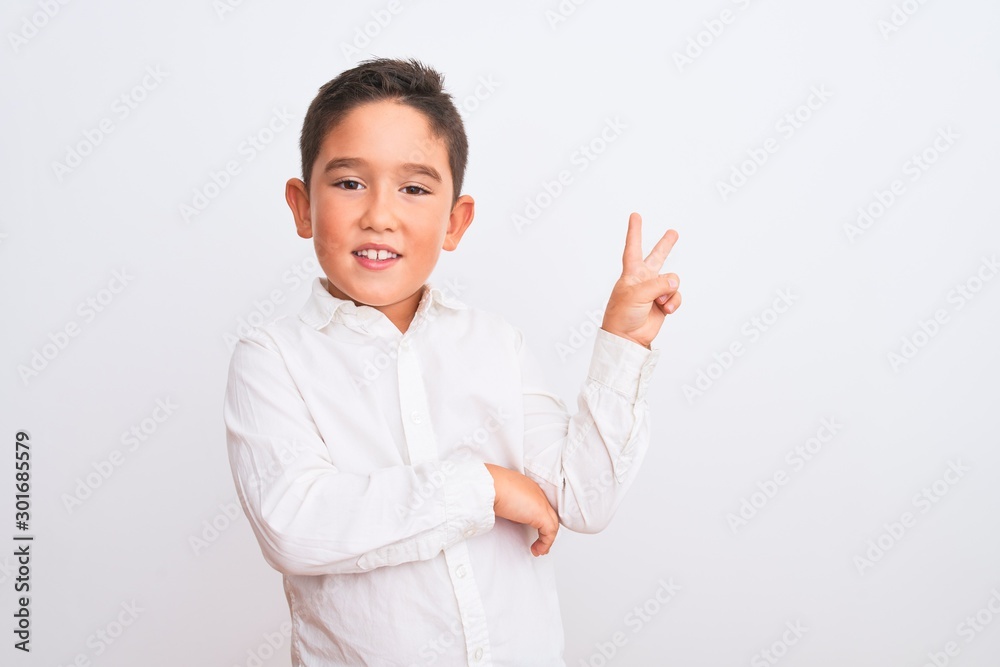 Beautiful kid boy wearing elegant shirt standing over isolated white background smiling with happy face winking at the camera doing victory sign. Number two. Beautiful kid boy wearing elegant shirt standing over isolated white background smiling with happy face winking at the camera doing victory sign. Number two.