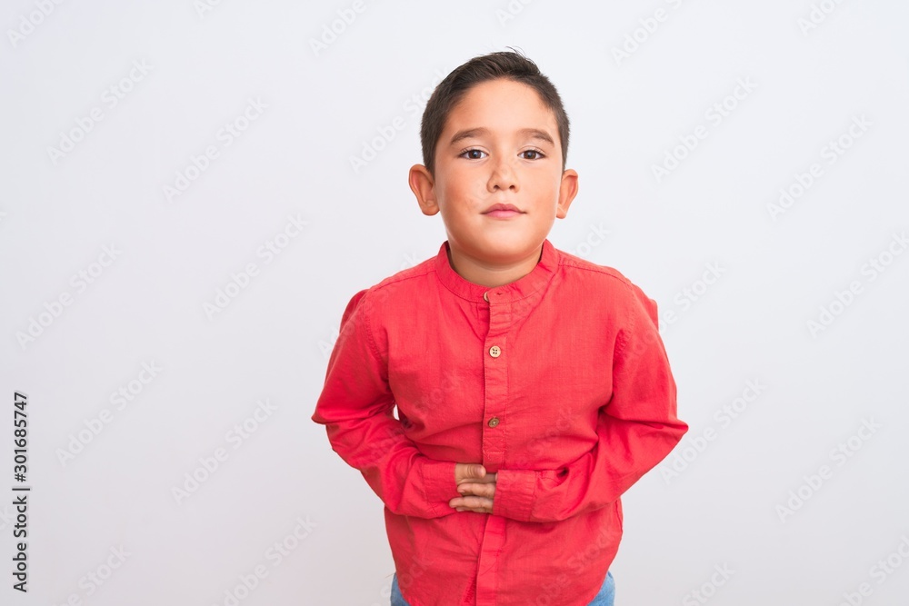 Beautiful kid boy wearing elegant red shirt standing over isolated white background with hand on stomach because indigestion, painful illness feeling unwell. Ache concept. Beautiful kid boy wearing elegant red shirt standing over isolated white background with hand on stomach because indigestion, painful illness feeling unwell. Ache concept.