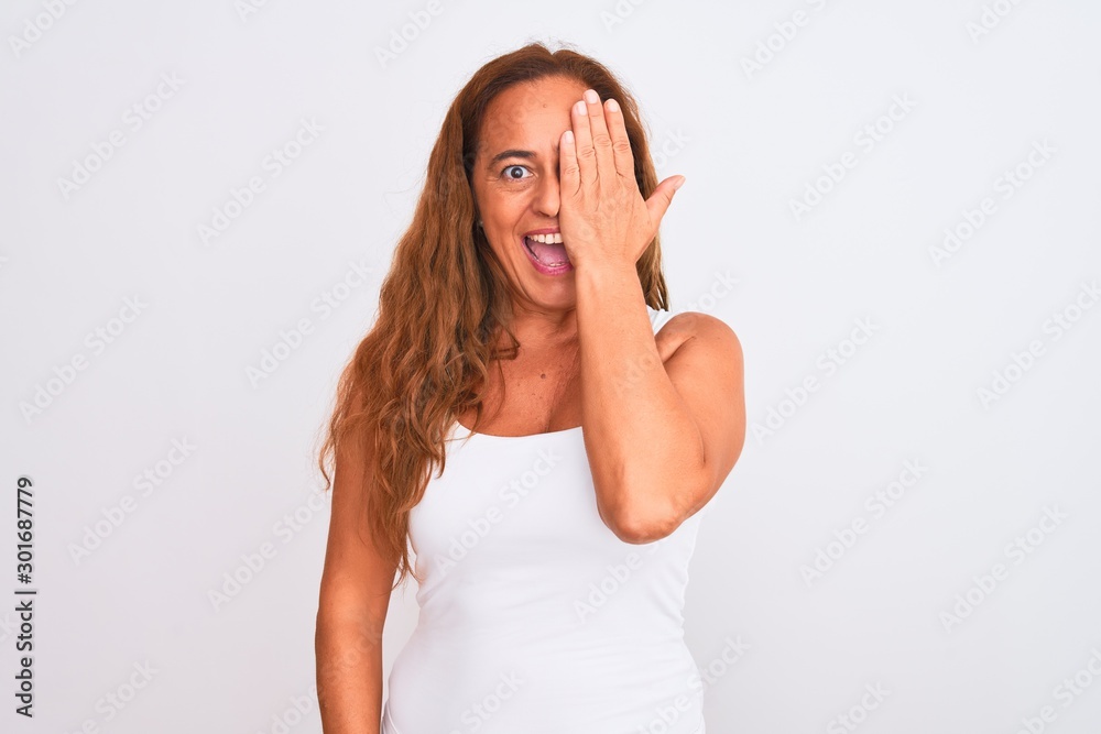 Middle age mature woman standing over white isolated background covering one eye with hand, confident smile on face and surprise emotion. Middle age mature woman standing over white isolated background covering one eye with hand, confident smile on face and surprise emotion.