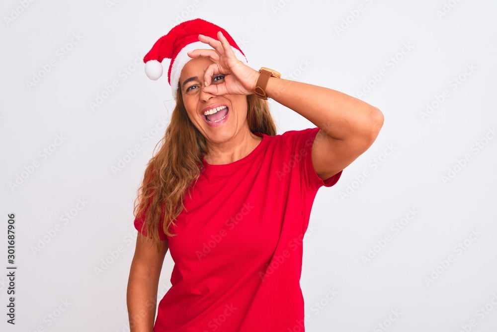 Middle age mature woman wearing christmas hat over isolated background doing ok gesture with hand smiling, eye looking through fingers with happy face.