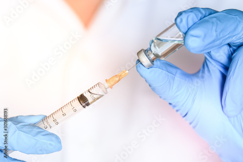 Nurse or doctor hand in blue glove holding flu, measles vaccine vial and syringe wiht needle for pregnant women vaccination, medicine and drug concept