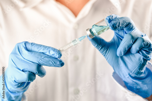 Nurse or doctor hand in blue glove holding flu, measles vaccine vial and syringe wiht needle for pregnant women vaccination, medicine and drug concept