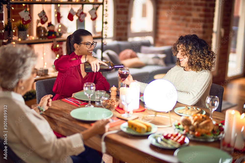 Beautiful group of women smiling happy and confident. Eating roasted turkey and serving wine on cup celebrating christmas at home