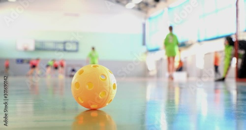 Floorball match of small floorball players. Children play floorball match in indoor hall. Intentionally focused on the ball in the foreground. Players in the background intentionally out of focus. photo