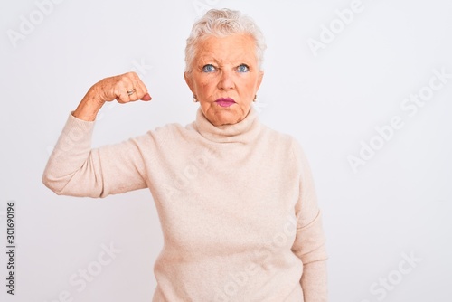 Senior grey-haired woman wearing turtleneck sweater standing over isolated white background Strong person showing arm muscle, confident and proud of power