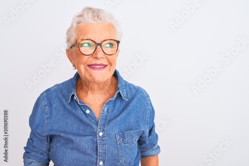 Senior grey-haired woman wearing denim shirt and glasses over isolated white background smiling looking to the side and staring away thinking.