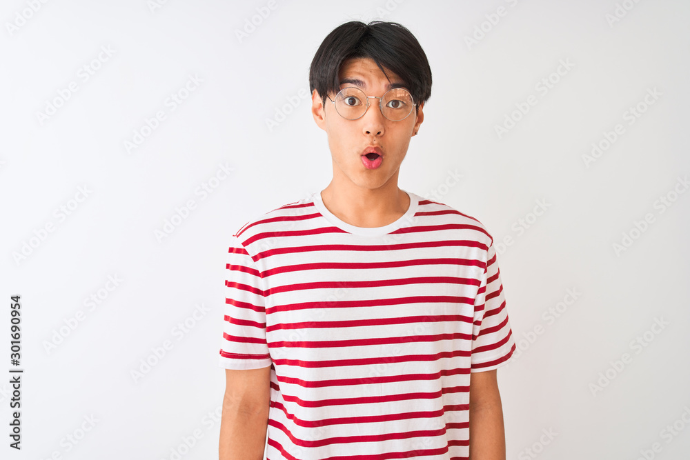 Young chinese man wearing glasses and striped t-shirt standing over isolated white background afraid and shocked with surprise expression, fear and excited face. Young chinese man wearing glasses and striped t-shirt standing over isolated white background afraid and shocked with surprise expression, fear and excited face.