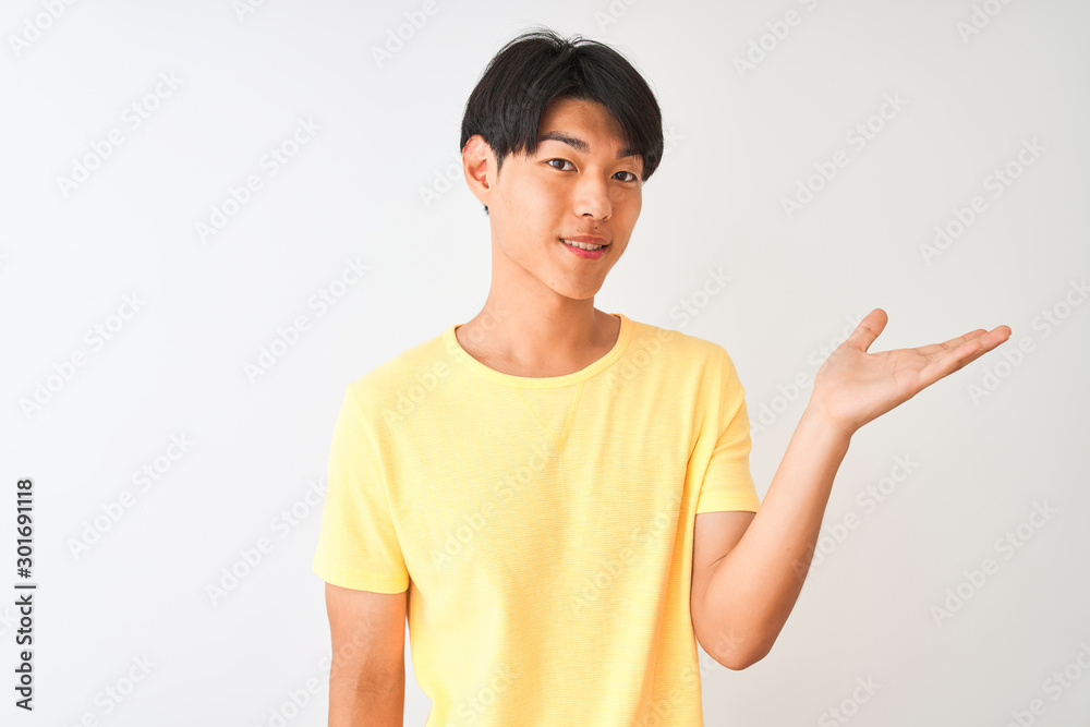 Chinese man wearing yellow casual t-shirt standing over isolated white background smiling cheerful presenting and pointing with palm of hand looking at the camera. Chinese man wearing yellow casual t-shirt standing over isolated white background smiling cheerful presenting and pointing with palm of hand looking at the camera.