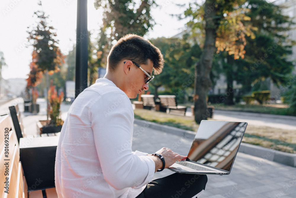 young stylish guy in shirt with phone and notebook on bench on sunny warm day outdoors, freelance young stylish guy in shirt with phone and notebook on bench on sunny warm day outdoors, freelance
