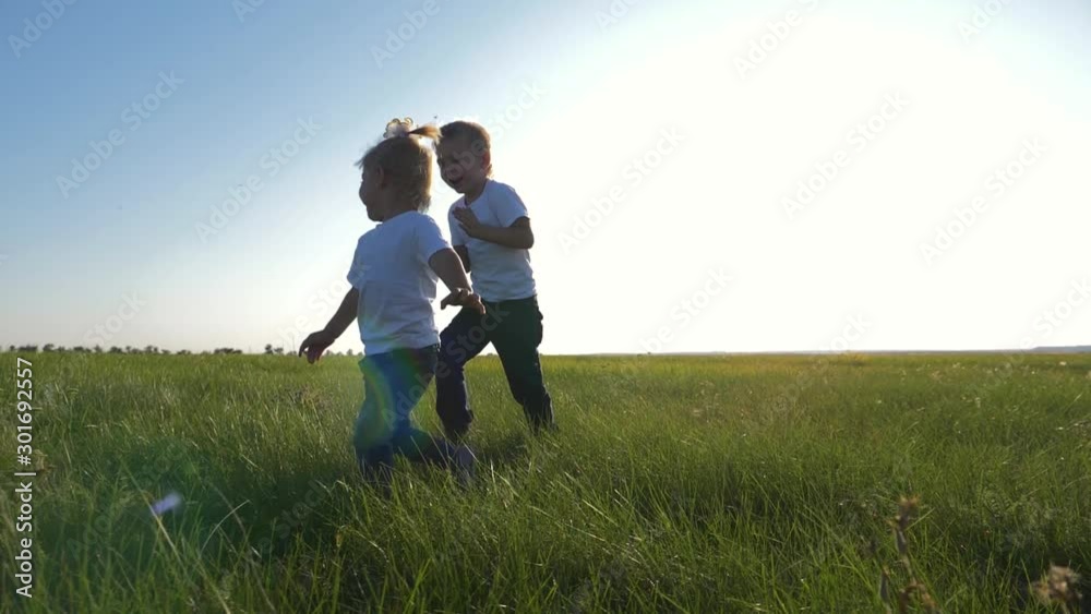 Two children in white t-shirts running on green fresh grass. Happy children enjoy life. The concept of teamwork. Two children in white t-shirts running on green fresh grass. Happy children enjoy life. The concept of teamwork.