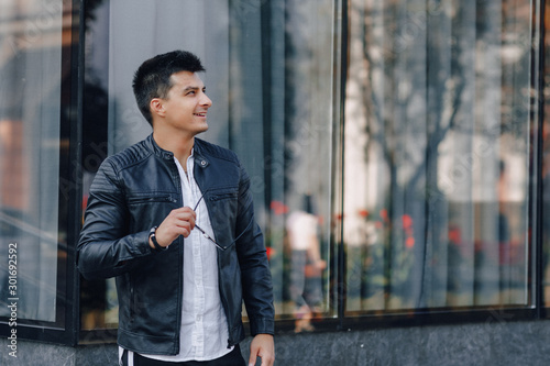 young stylish guy in glasses in black leather jacket on glass background