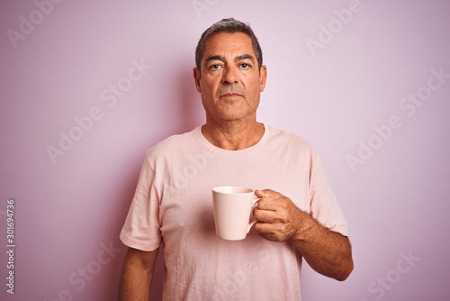 Handsome middle age man holding cup of coffee standing over isolated pink background with a confident expression on smart face thinking serious