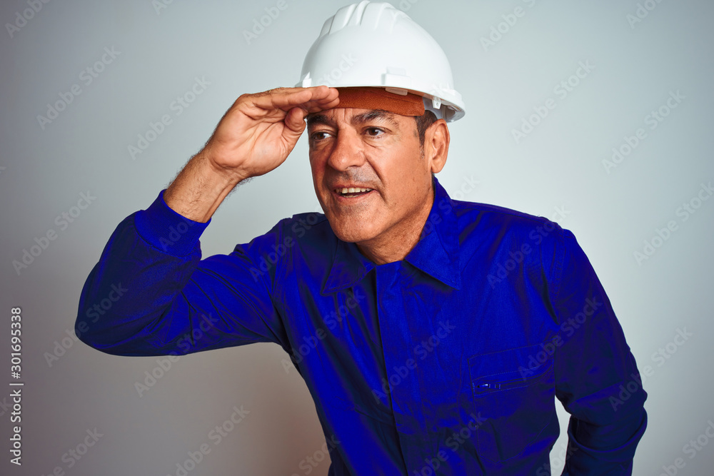Handsome middle age worker man wearing uniform and helmet over isolated white background very happy and smiling looking far away with hand over head. Searching concept. Handsome middle age worker man wearing uniform and helmet over isolated white background very happy and smiling looking far away with hand over head. Searching concept.