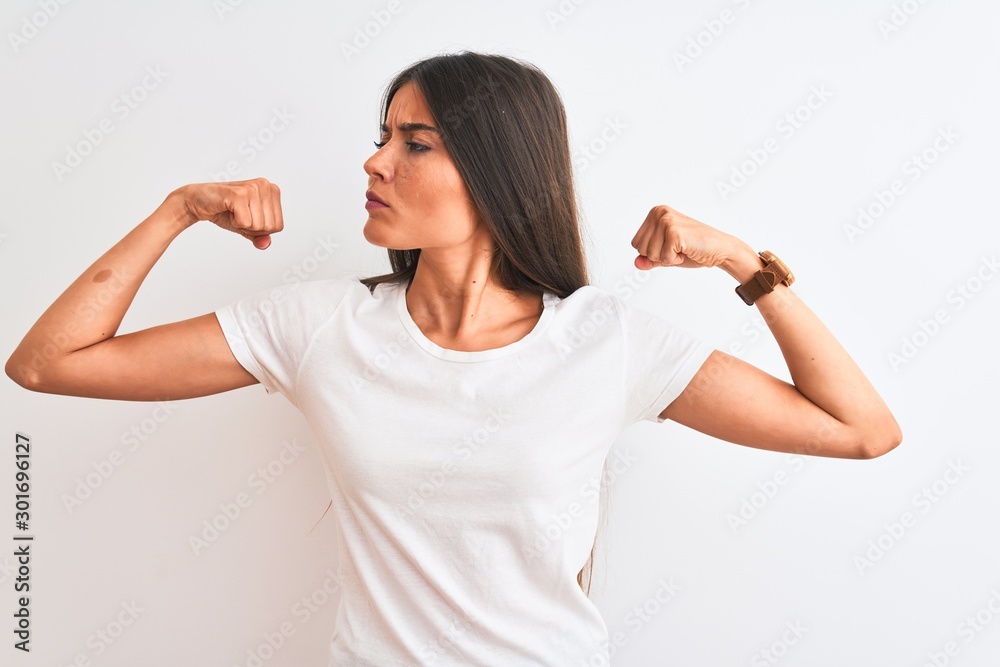 Young beautiful woman wearing casual t-shirt standing over isolated white background showing arms muscles smiling proud. Fitness concept. Young beautiful woman wearing casual t-shirt standing over isolated white background showing arms muscles smiling proud. Fitness concept.