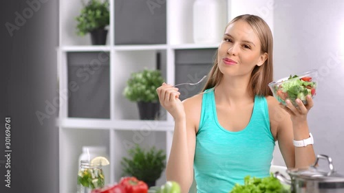 Attractive dieting girl eating fresh organic vegetable salad in kitchen at home looking at camera photo