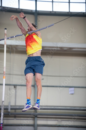 Pole vaulting indoors - a man falling down after jumping over the bar