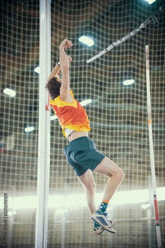 Pole vaulting indoors - a sportive man falling down after the jump - bright lights on the background