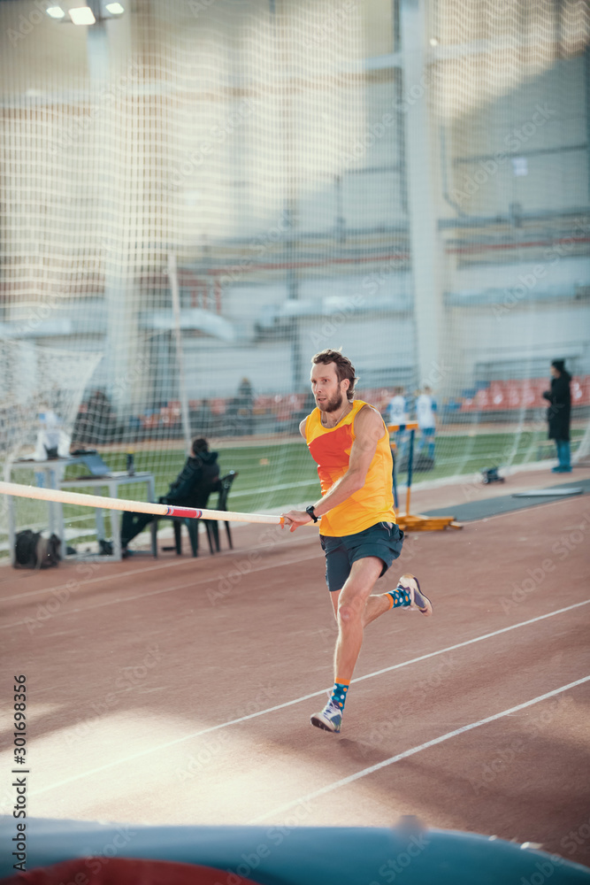 Pole vaulting in the sports stadium - a sportive man running on the track