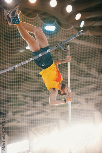 Pole vaulting training in the sports stadium - an athletic man jumping over the bar