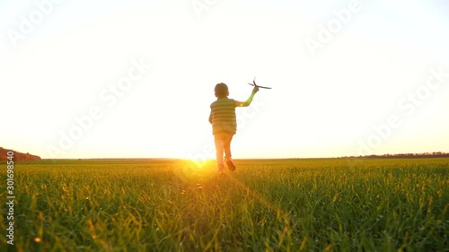 A happy little boy runs across a green meadow playing with a toy airplane, imagining flying. photo