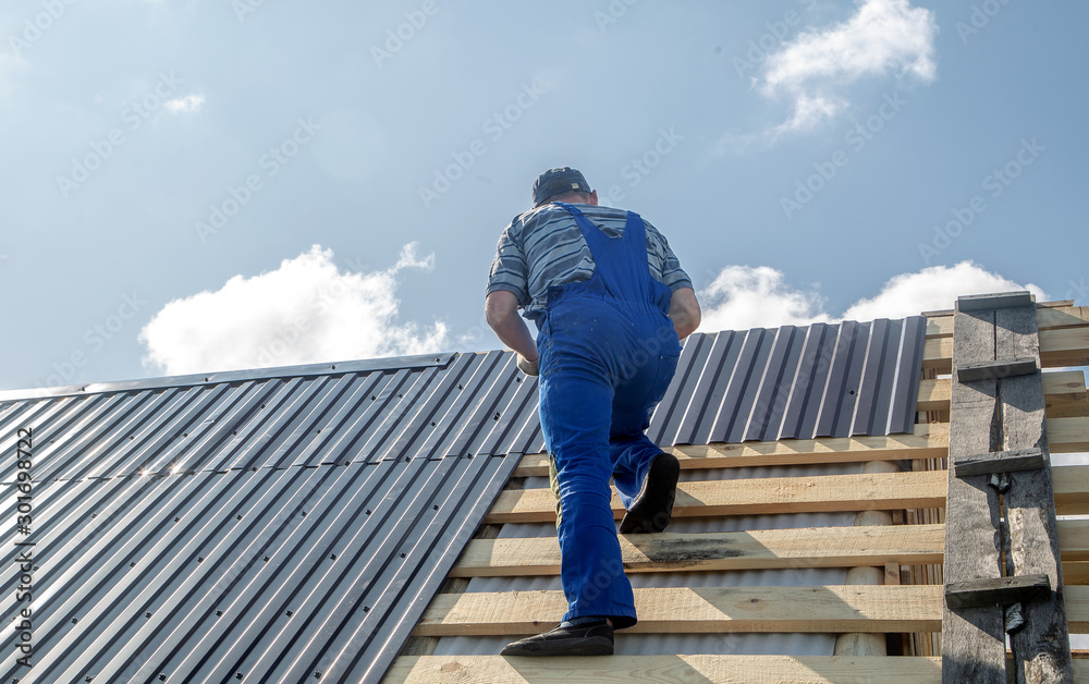 male builder performs work on the roof, fastens corrugated sheets О male builder performs work on the roof, fastens corrugated sheets О