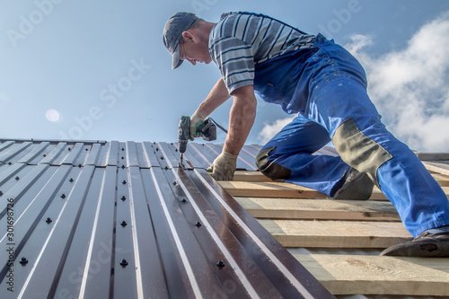 male builder performs work on the roof, fastens corrugated sheets О