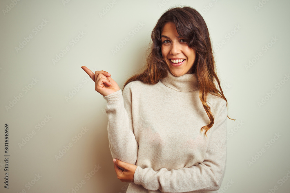 Young beautiful woman wearing winter sweater standing over white isolated background with a big smile on face, pointing with hand finger to the side looking at the camera. Young beautiful woman wearing winter sweater standing over white isolated background with a big smile on face, pointing with hand finger to the side looking at the camera.