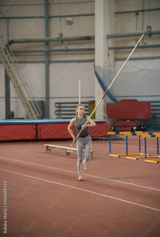 Pole vaulting in the sports stadium - young sportive woman with ponytail in grey leggins running with a pole