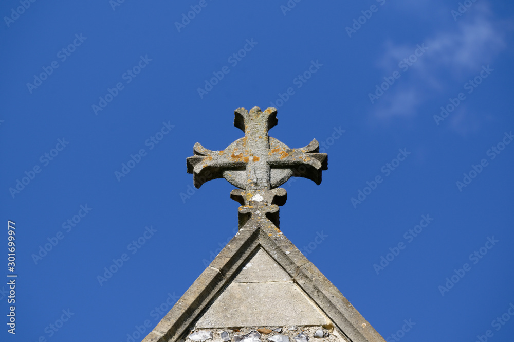 An old cross sits against a blue sky atop a church