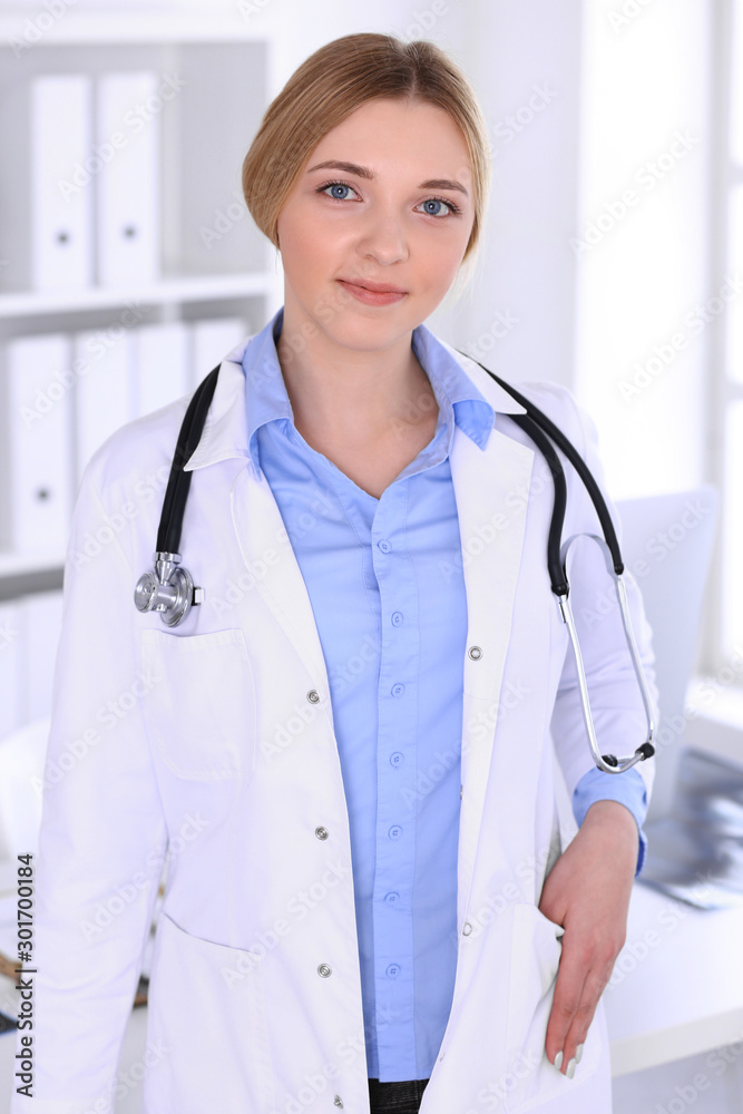 Young woman doctor at work in hospital looking at camera. Blue colored blouse of therapist looks good. Medicine and healthcare concept Young woman doctor at work in hospital looking at camera. Blue colored blouse of therapist looks good. Medicine and healthcare concept