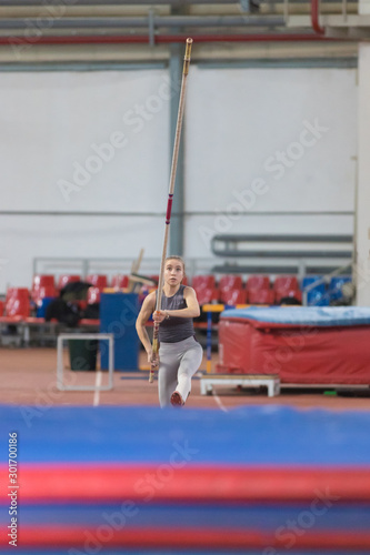 Pole vaulting - woman in a gray suit is running with pole in hands