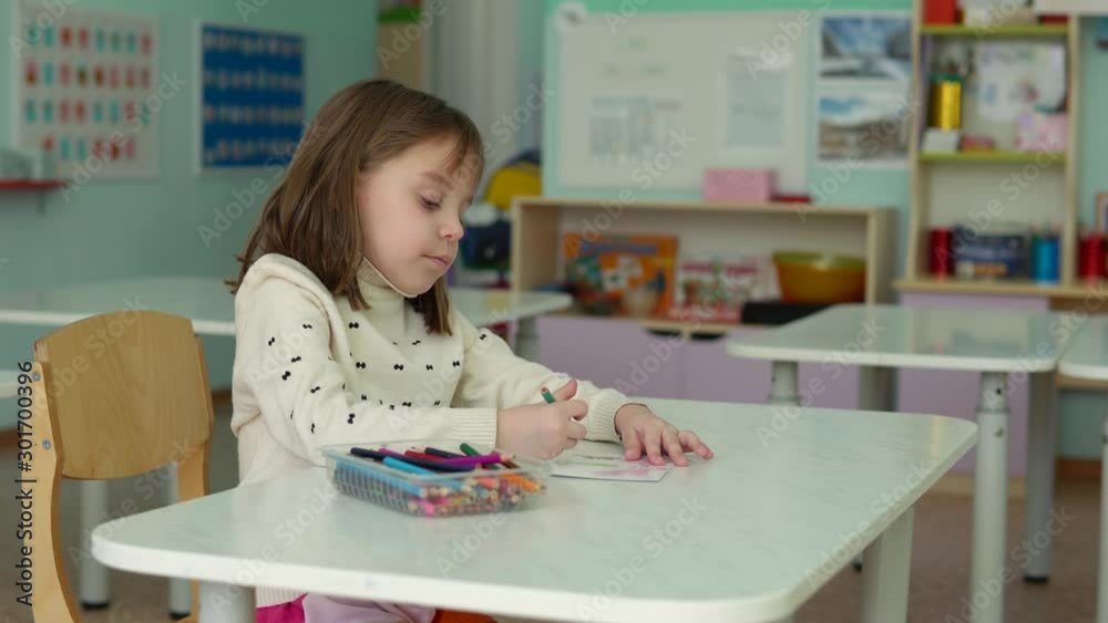 Lonely girl in kindergarten. Child, girl 5-6 years old, draws, sitting at the table. Lonely girl in kindergarten. Child, girl 5-6 years old, draws, sitting at the table.