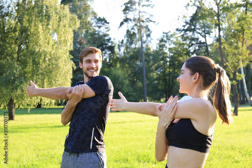 Young couple stretching muscles outdoors in park at sunny day.