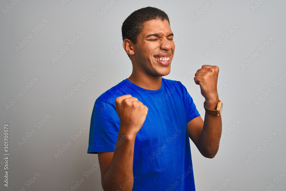 Young handsome arab man wearing blue t-shirt standing over isolated white background very happy and excited doing winner gesture with arms raised, smiling and screaming for success Young handsome arab man wearing blue t-shirt standing over isolated white background very happy and excited doing winner gesture with arms raised, smiling and screaming for success