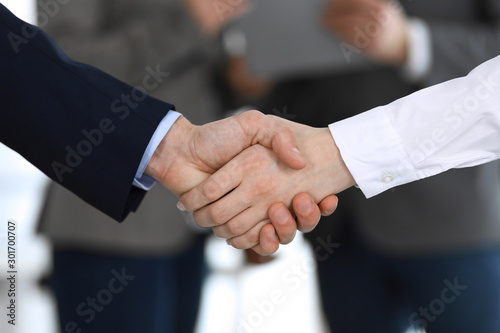 Business people shaking hands while standing with colleagues after meeting or negotiation, close-up. Group of unknown businessmen and women in modern office. Teamwork, partnership and handshake