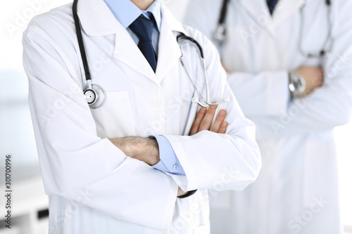 Doctor man standing straight and crossed arms with colleague at background, close-up. Group of doctors. Perfect medical service in clinic. Medicine and healthcare concepts. Toned picture