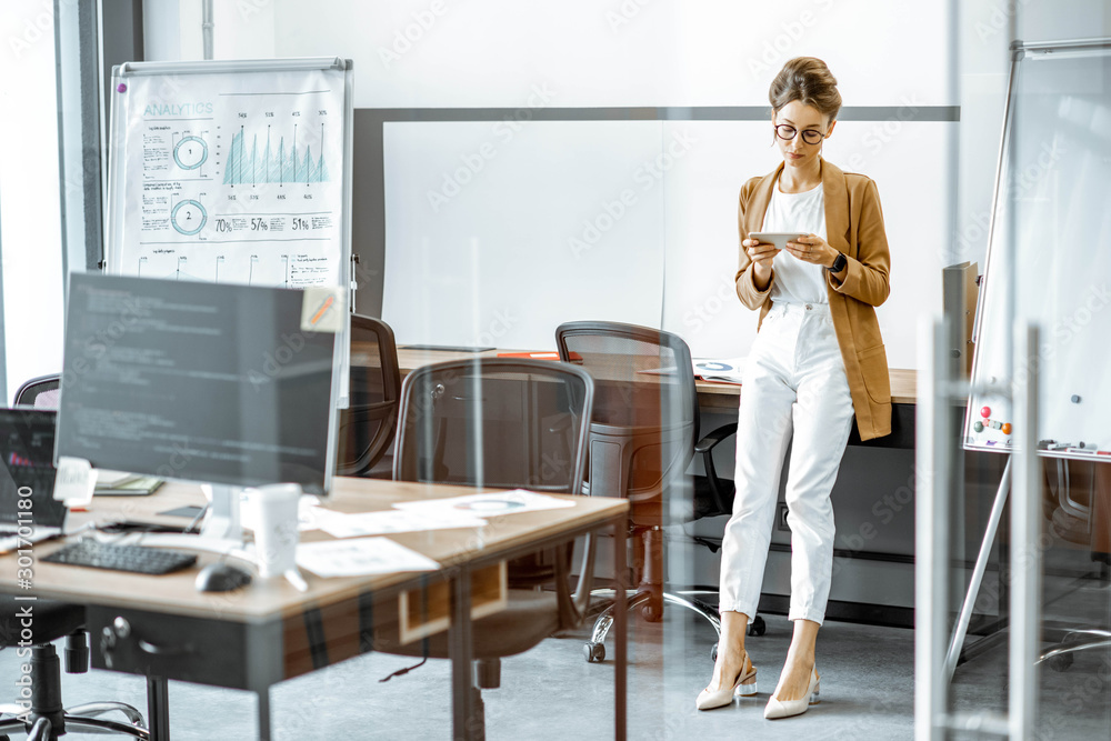 Young business woman preparing for a presentation, standing alone with phone near flipchart in the modern office or coworking space