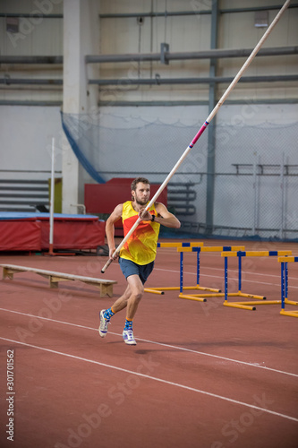 Pole vaulting - man in yellow shirt is running with pole in hands © KONSTANTIN SHISHKIN