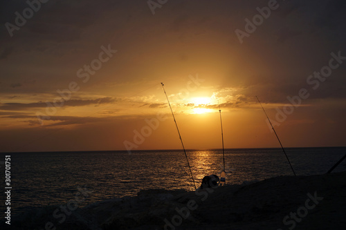 Fishing rods by the sea on a background of sunset and sea. Amazing warm calm evening on the seashore during a wonderful summer vacation at the seaside resort. 