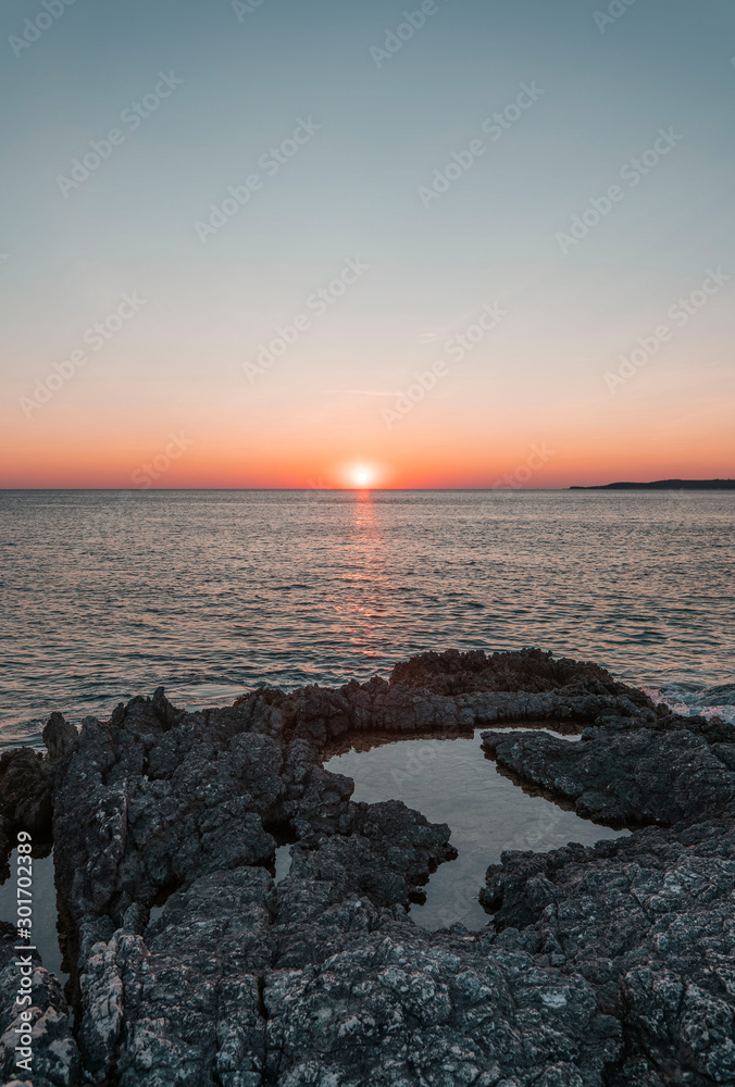 Beautiful Adriatic sea sunset with waves breaking onto stone beach 