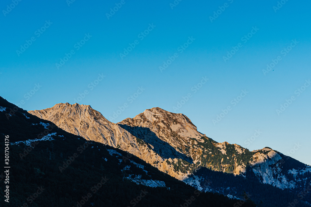 Beautiful sunset view of a mountain alpine landscape of Totes Gebirge, Austria. High alpine peaks in yellow and orange evening light. Rocky summit and rock walls of alpine peaks. Blue sky.