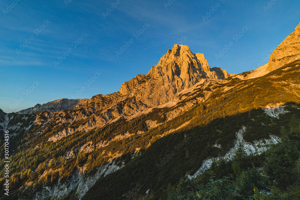 Fantastic view of a alpine mountain landscape of Totes Gebirge and the summit of Spitzmauer. Big rock wall, blue sky and mountains lid with orange sun. Sunrise or sunset mountain landscape, Austria.