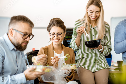 Картината върху платно Group of diverse colleagues eating takeaway salad, sitting together and having f