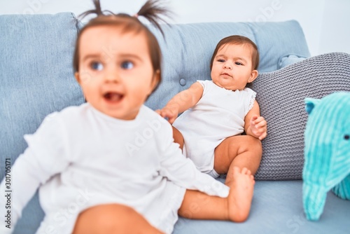 Beautiful infant happy girls playing together at home kindergarten sitting on the sofa