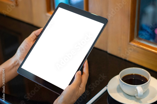 Mockup image of business woman hands holding black tablet computer pc  with blank white screen with pencil and  cup of hot black coffee on table at cafe.