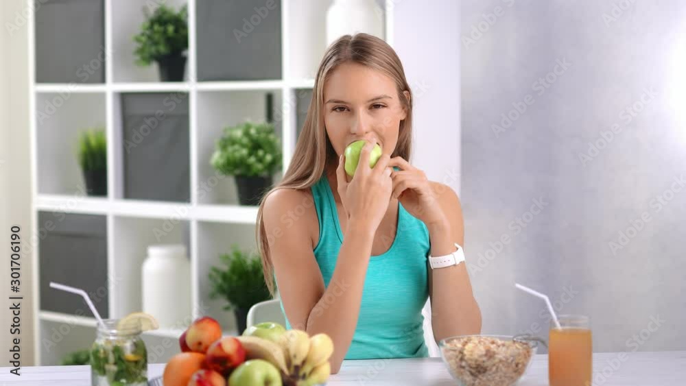 Attractive young woman eating fresh green apple in kitchen at home Attractive young woman eating fresh green apple in kitchen at home