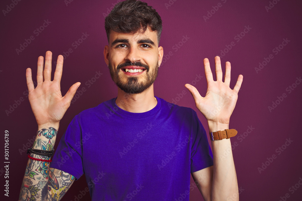 Young man with tattoo wearing t-shirt standing over isolated purple background showing and pointing up with fingers number ten while smiling confident and happy. Young man with tattoo wearing t-shirt standing over isolated purple background showing and pointing up with fingers number ten while smiling confident and happy.