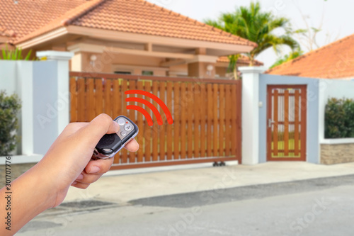 Hand holding and showing remote control to open or close the automatic electric wooden gate with modern home blurred background. Security and save time concept. photo